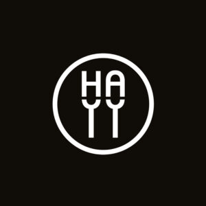 Logotipo circular de la Asociación de Hosteleros de Alcalá de Guadaíra con las iniciales HA y dos tenedores sobre fondo negro.