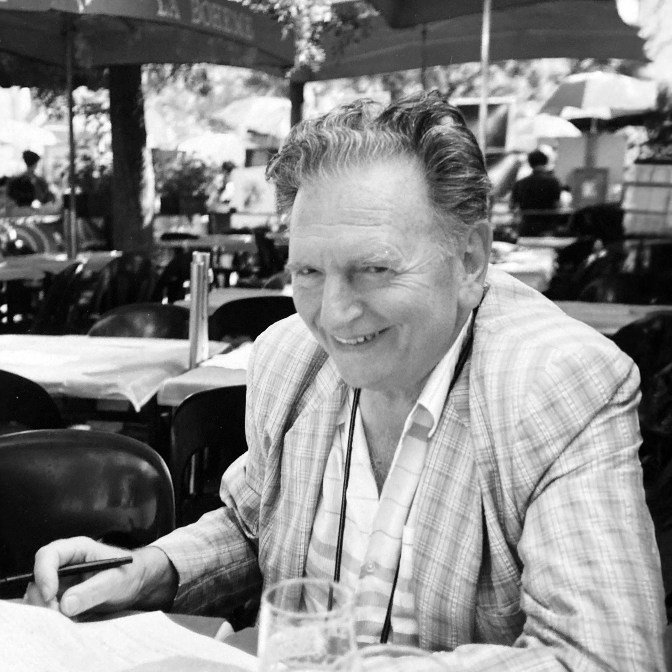 Jacques Devillers sonriente en una terraza de París con papeles de trabajo.