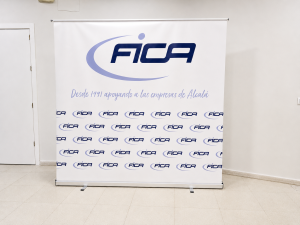 Roll-up del branding corporativo de FICA con logotipo azul y lavanda, mensaje institucional y patrón gráfico repetido.